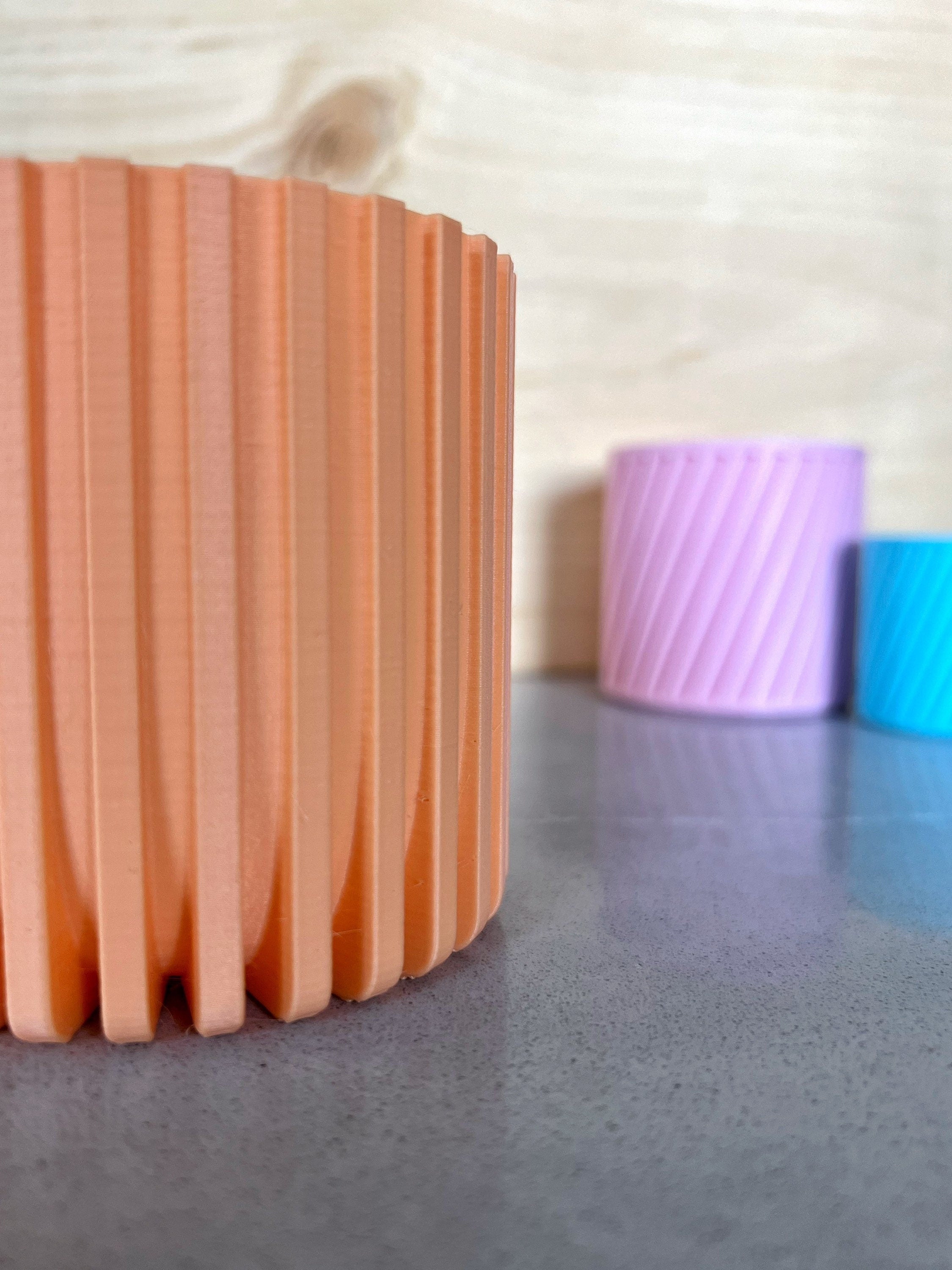 Peach 3D printed Modern Fluted Planter on a gray surface with lavender and blue planters behind it