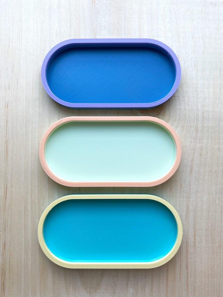 Three empty two-tone oval trays in blue on blue, mint and peach, and teal and yellow, top view