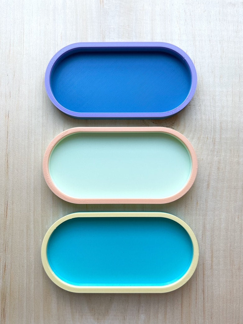 Three empty two-tone oval trays in blue on blue, mint and peach, and teal and yellow, top view