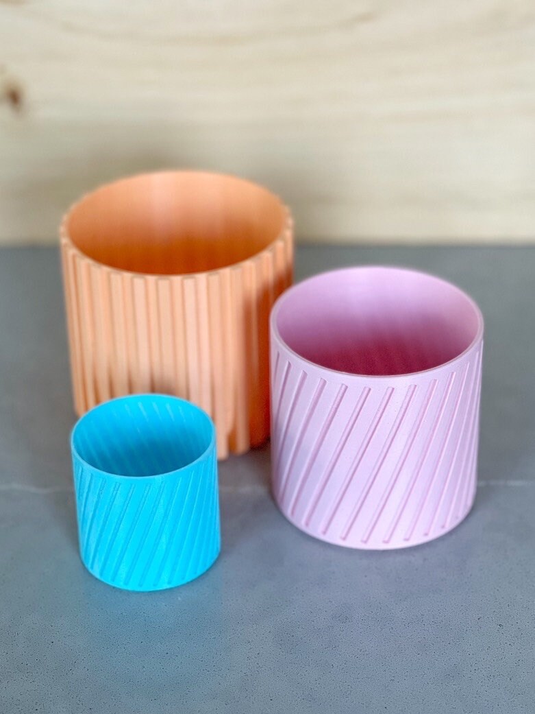 Peach, pink, and small blue diagonal stripe 3D printed planters on a gray surface