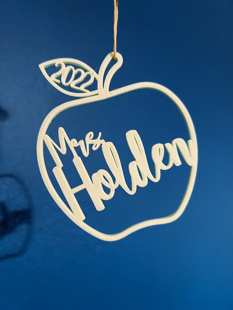 Personalized apple teacher ornament reading Mrs Holden 2022 against a navy wall