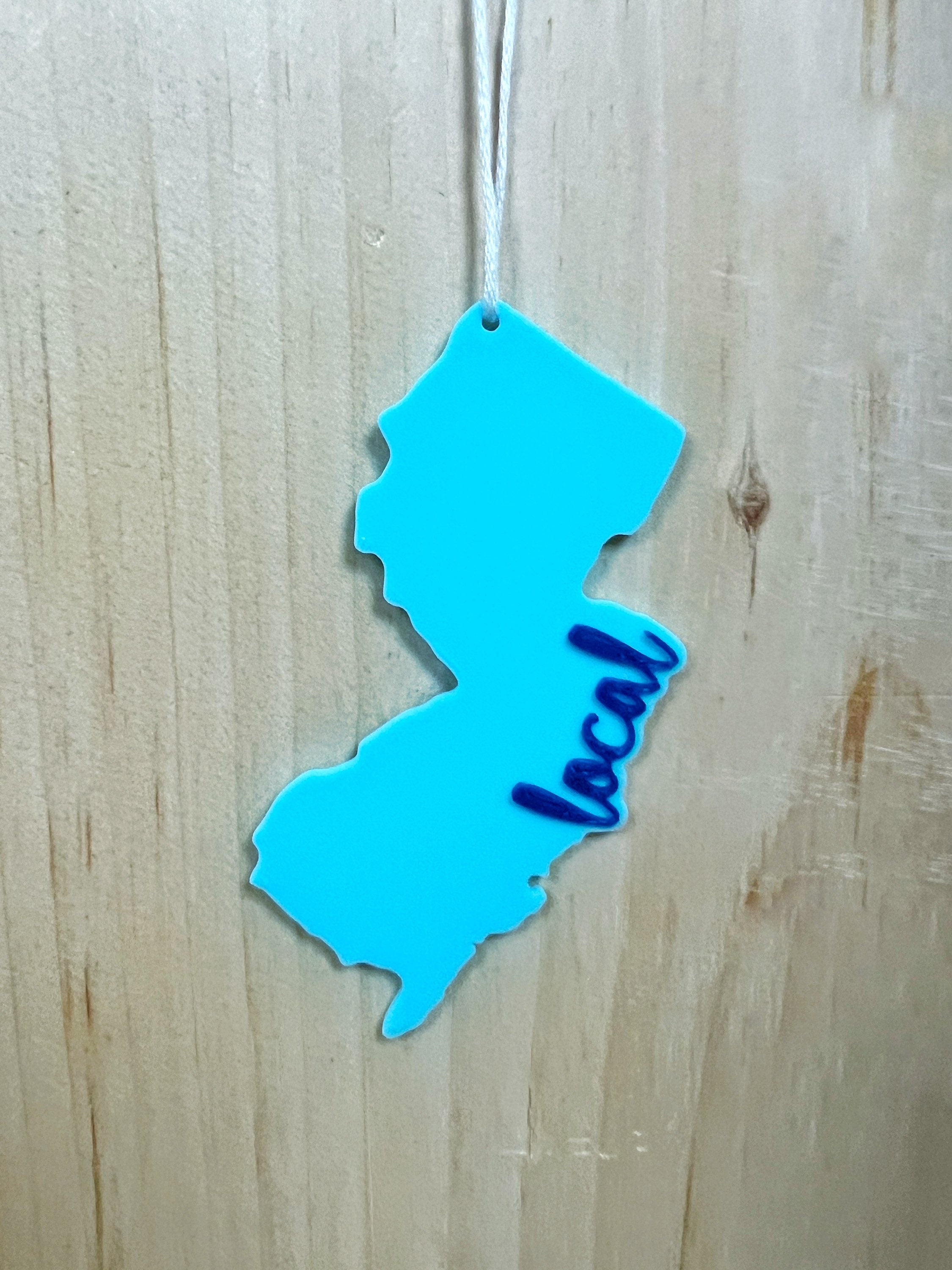 Light blue New Jersey local ornament with navy script hanging against a wood background