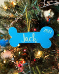 Personalized 3D printed dog bone ornament reading Jack 2022, light blue with mint lettering, hanging on a lit Christmas tree