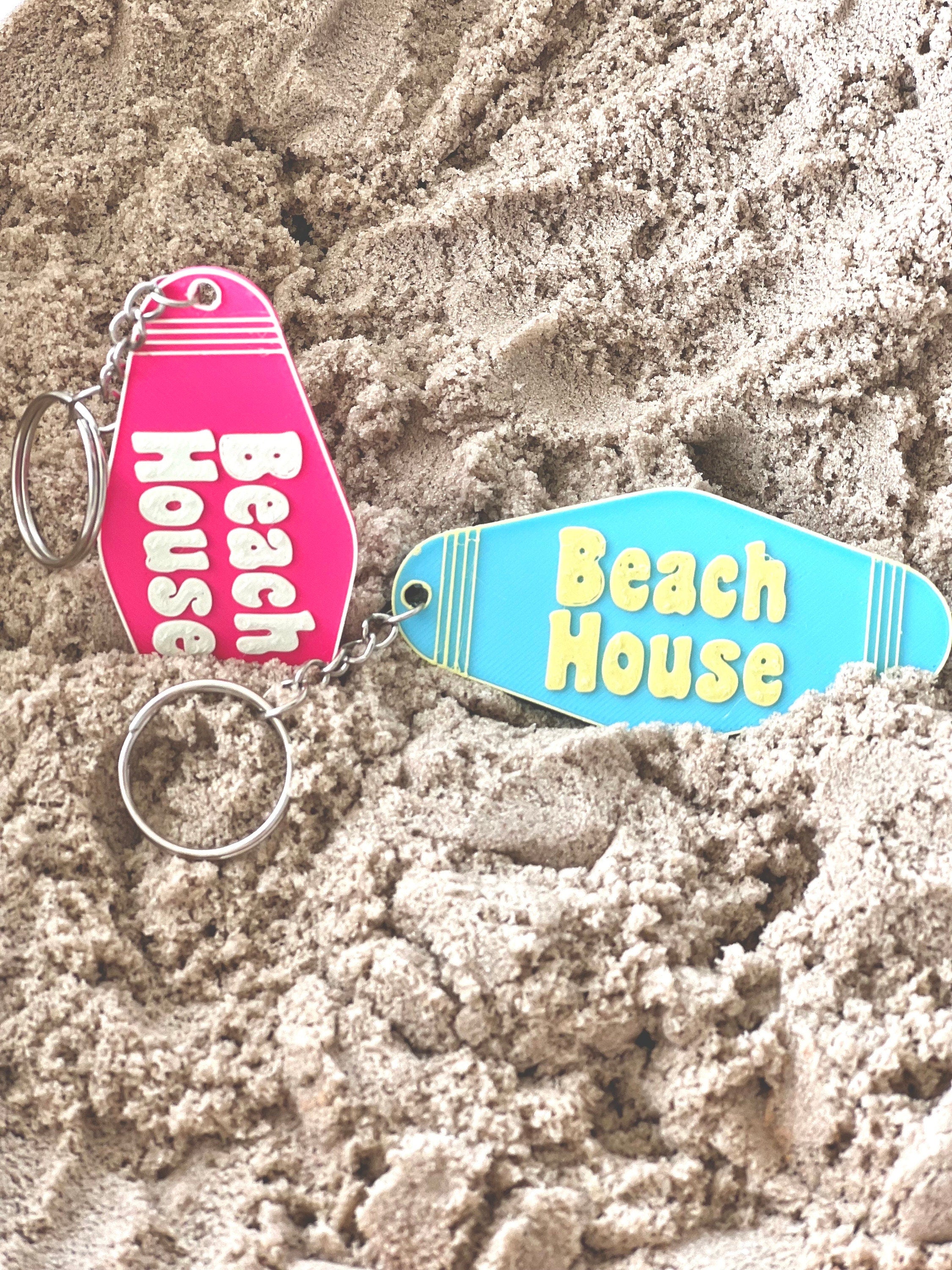 Pink and blue 3D printed Beach House keychains lying in beach sand