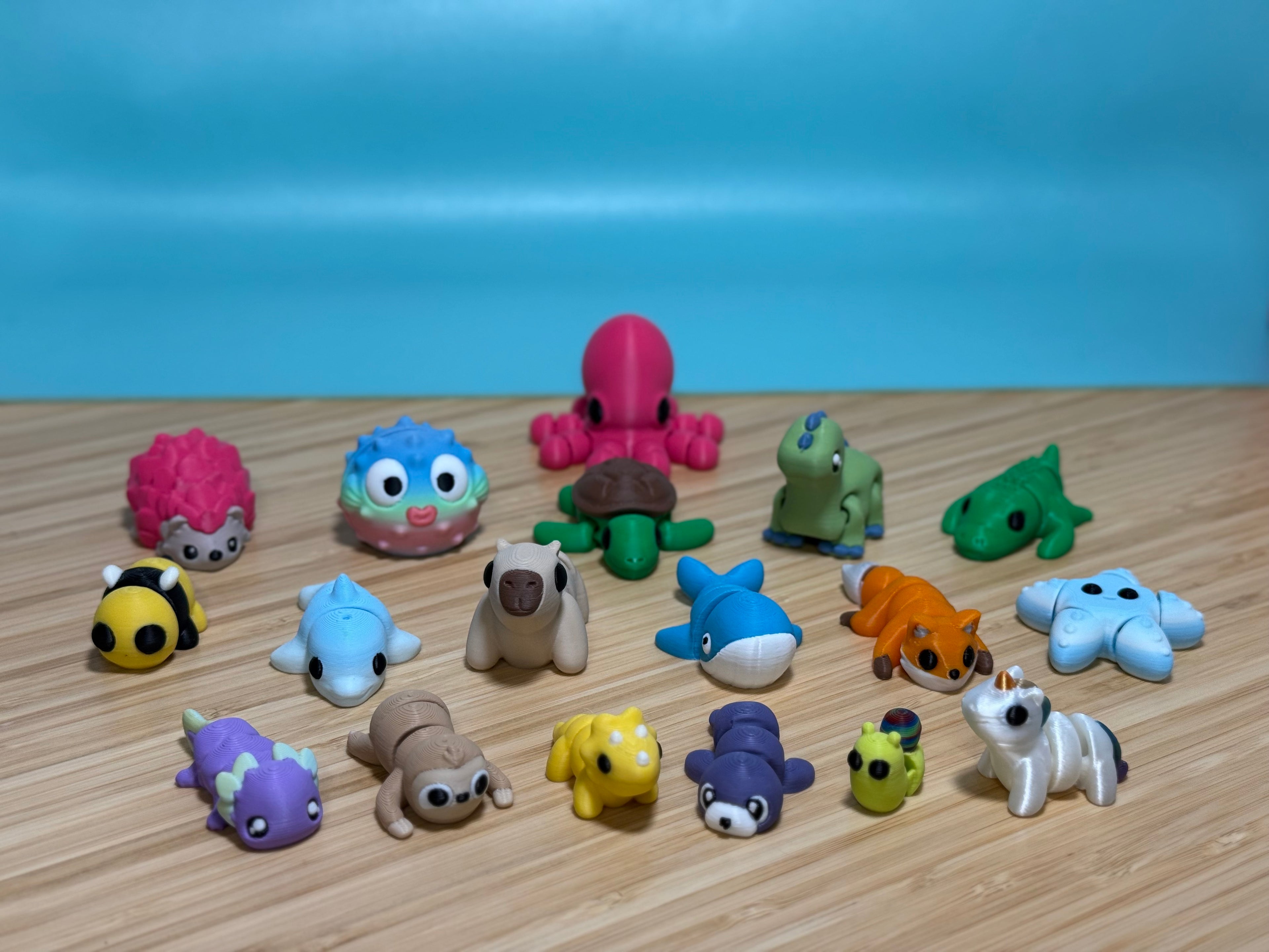 Tan 3D printed Mini Flexi Capybara in the middle of the full set of 18 Mini Flexi animals on a wood desk